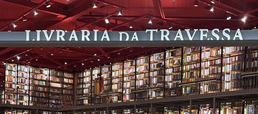Letreiro da Livraria da Travessa e estantes de livros sob o teto vermelho no interior da loja do Shopping Iguatemi.