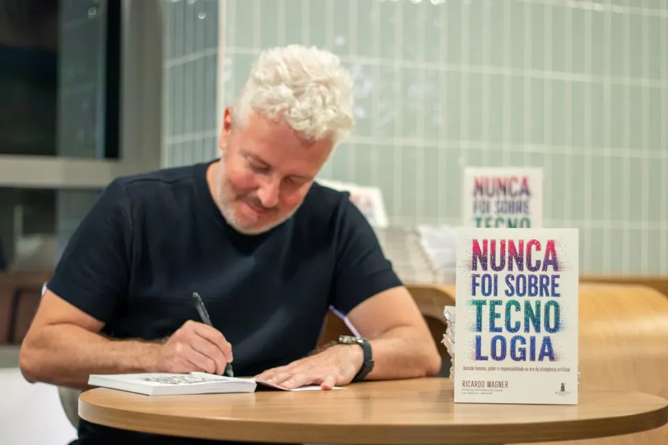 Ricardo Wagner sorrindo enquanto autografa um exemplar, com Nunca Foi Sobre Tecnologia em pé sobre a mesa.